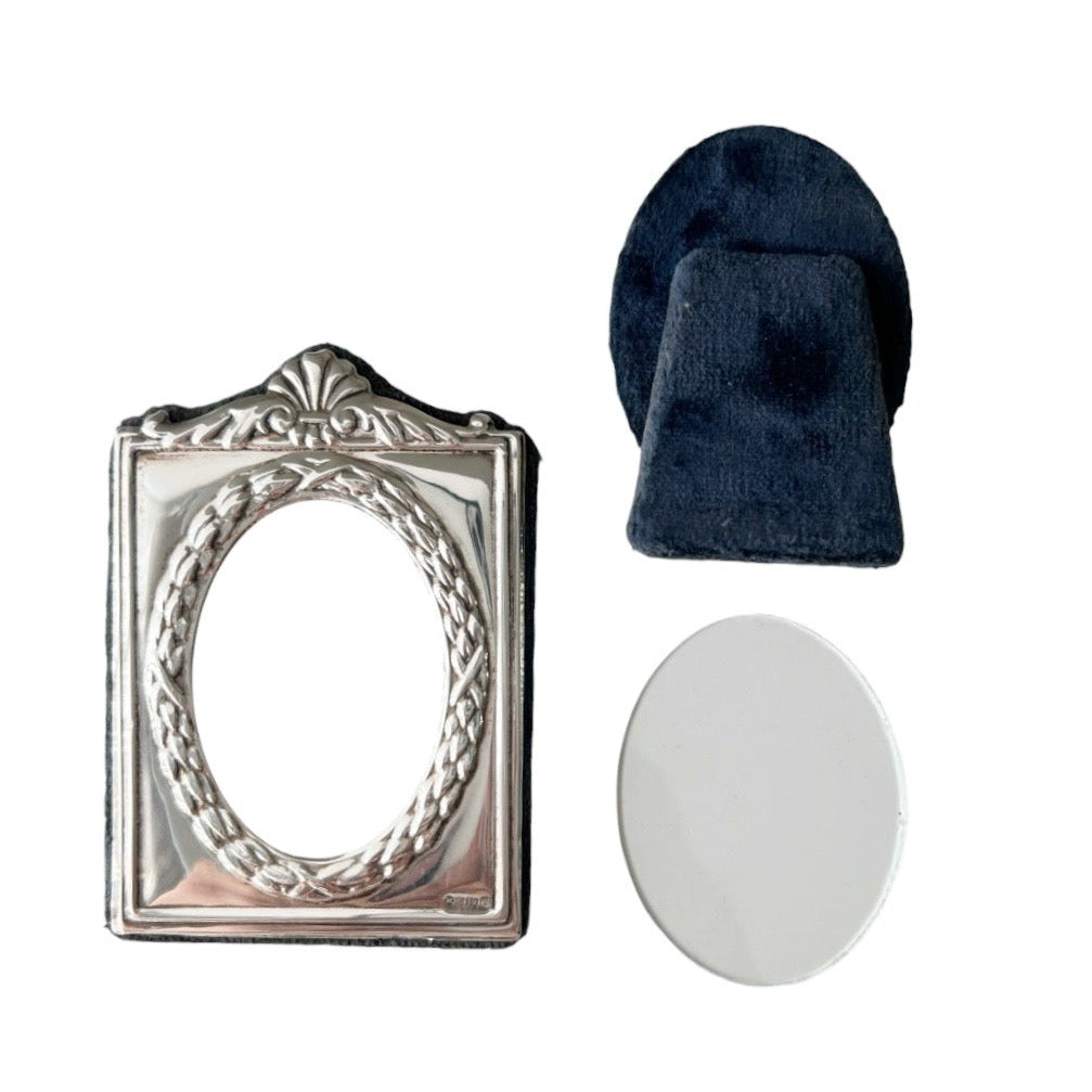 An ornate silver oval picture frame with a decorative crest and rope border,  on a plain white background.