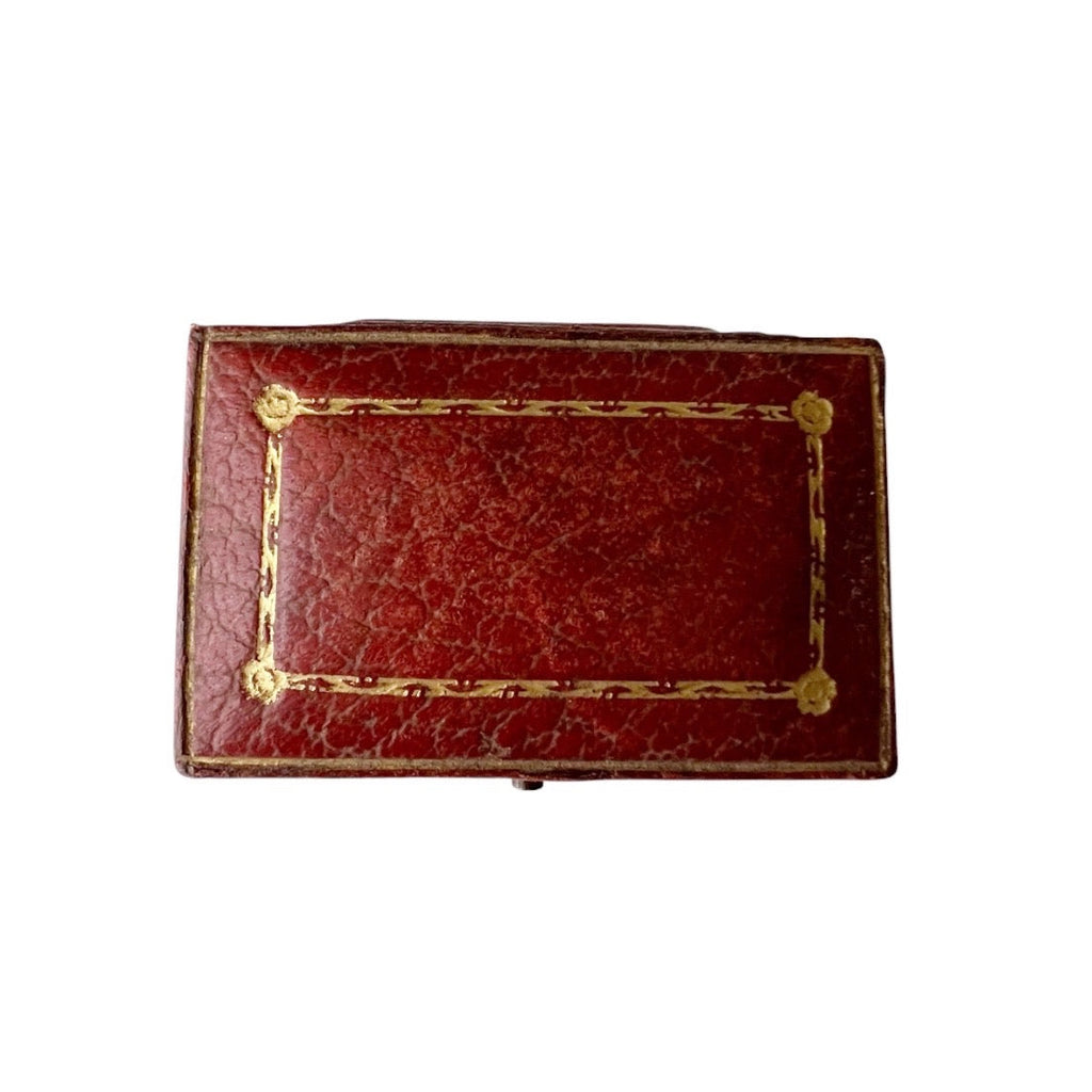 Antique rectangular red leather case with gold-toned metal corner studs and a gold border line on the lid, shown against a plain white background.