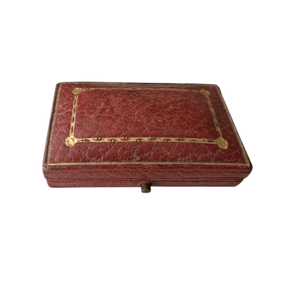Antique rectangular red leather case with gold decorative border detailing and corner accents, shown on a plain white background.
