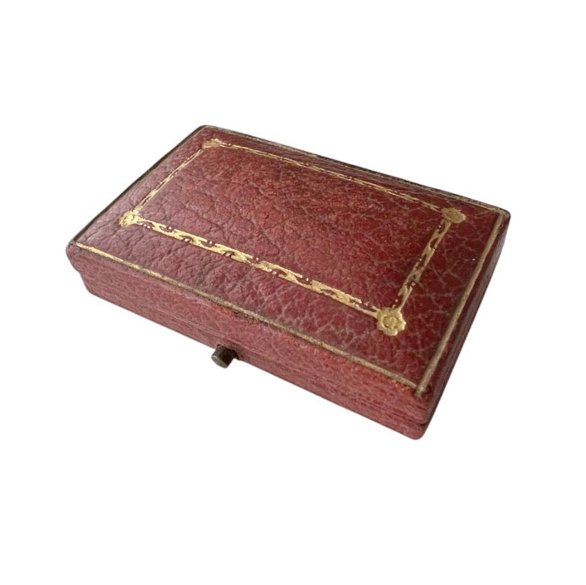 Antique rectangular red leather case with gold foil decorative borders and corner accents, shown on a plain white background.