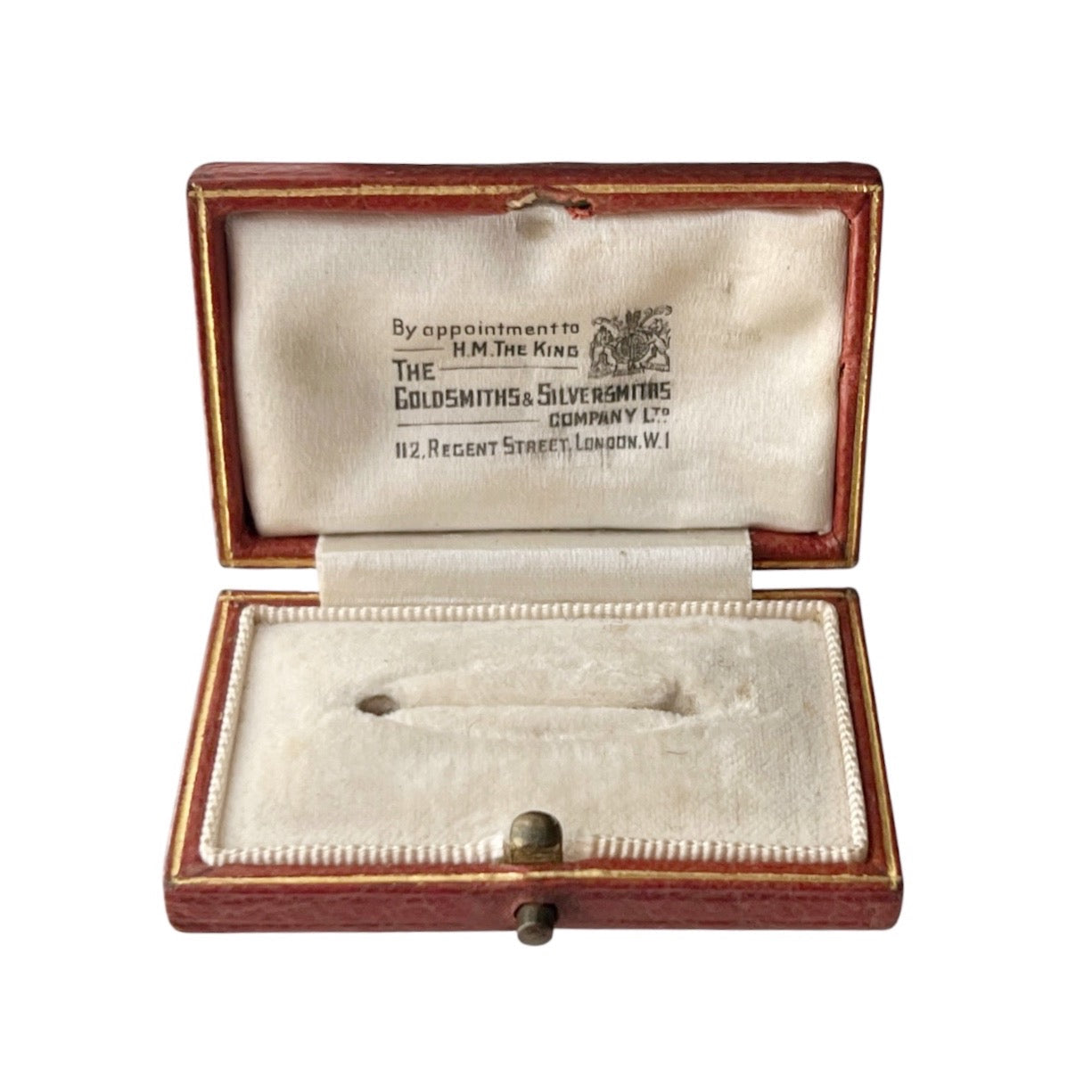 An open antique leather brooch  box with a cream velvet-lined interior, displaying a small silver-toned pin. The inside lid features printed branding text for 'The Goldsmiths & Silversmiths Company Ltd'.